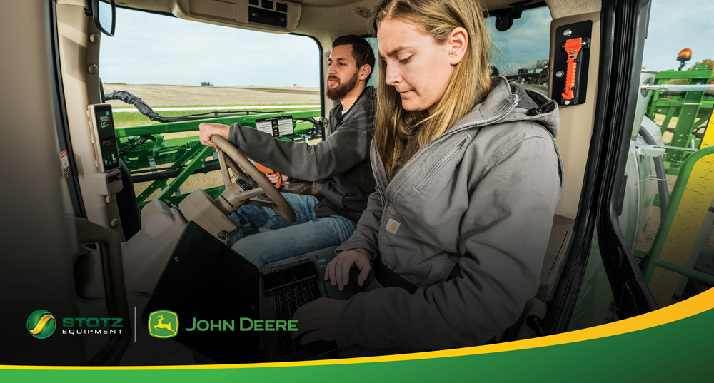 Image of two people in a sprayer cab, one on a laptop, one operating.